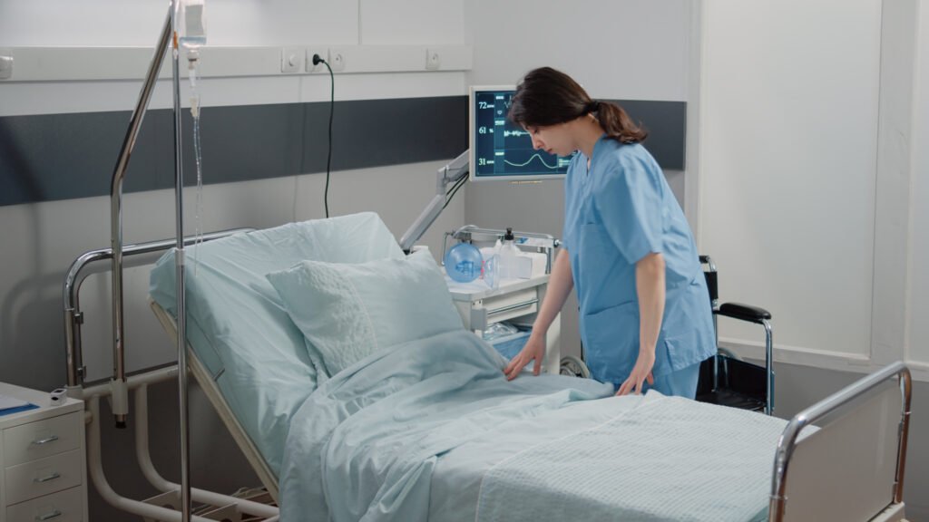 Nurse making bed in hospital ward with healthcare equipment
